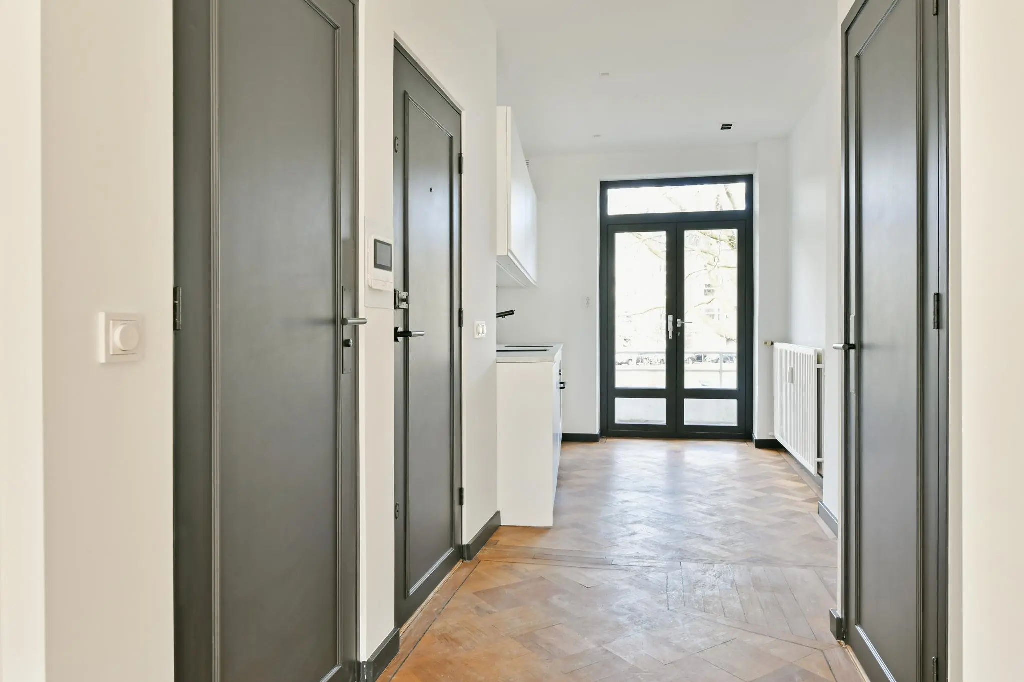 Lichte hal met houten visgraatvloer, zwarte deuren en openslaande deuren naar balkon aan de Cornelis Dopperkade.